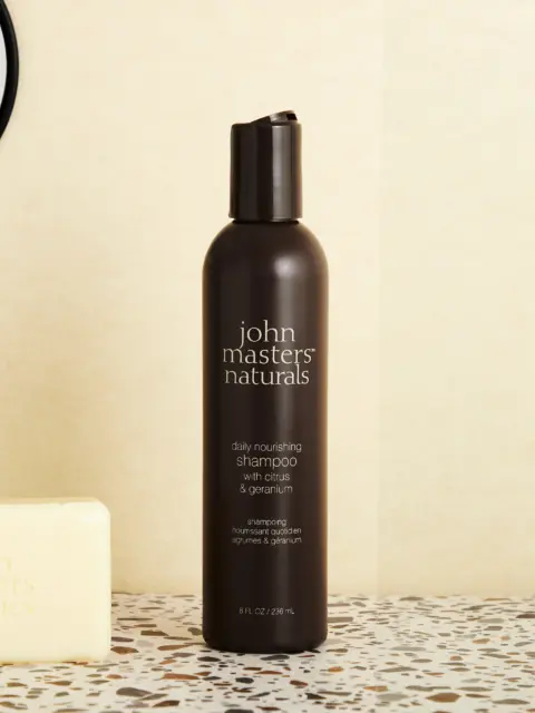 Brown bottle of John Masters Naturals shampoo with citrus and geranium, next to a soap bar.