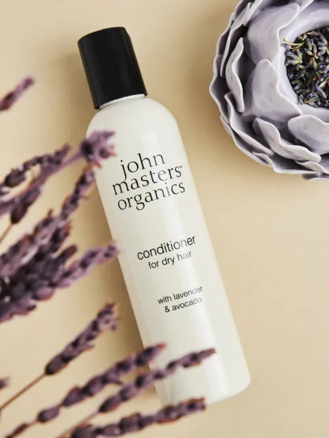 John Masters Organics conditioner for dry hair with lavender and avocado, next to lavender flowers.