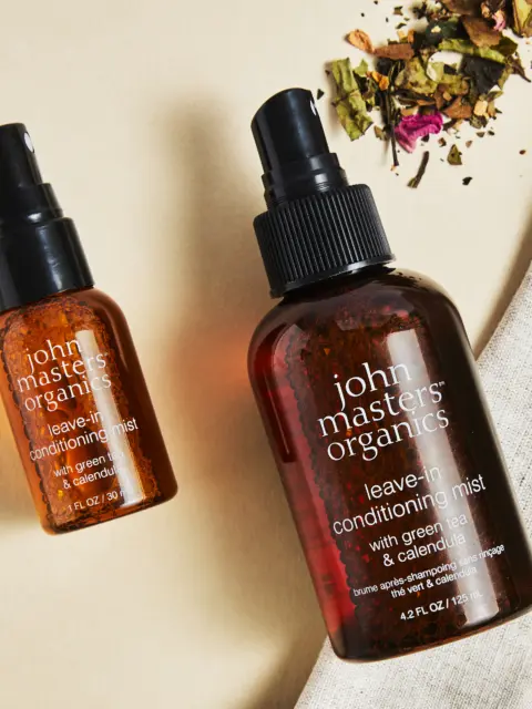 Two bottles of John Masters Organics leave-in conditioning mist on a beige surface.