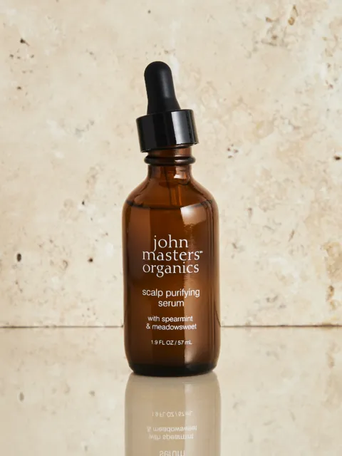 Brown bottle of John Masters Organics scalp purifying serum with dropper on stone background.