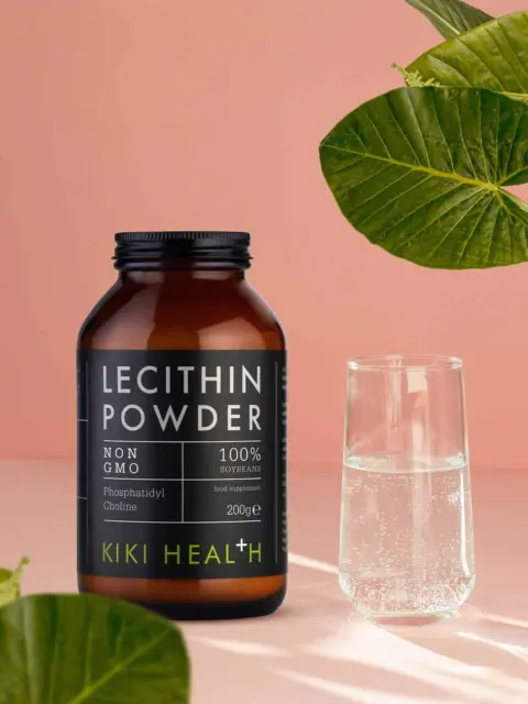 Lecithin powder jar and glass of water on pink background with green leaves.