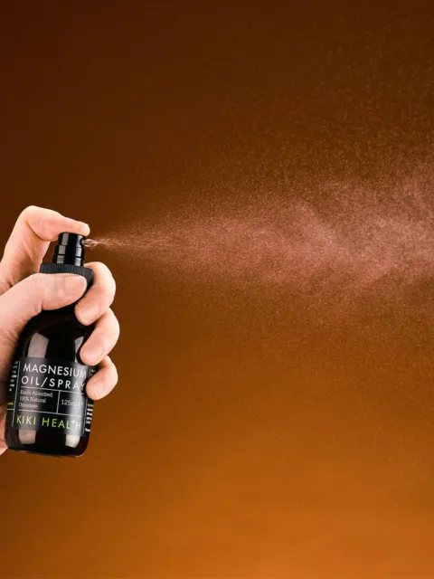 Hand spraying magnesium oil from a black bottle against a brown background.