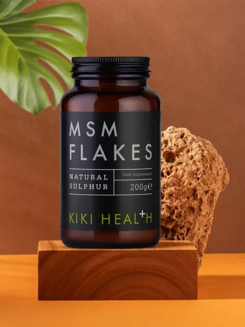 MSM Flakes jar, 200g, on wooden block with plant and stone background.