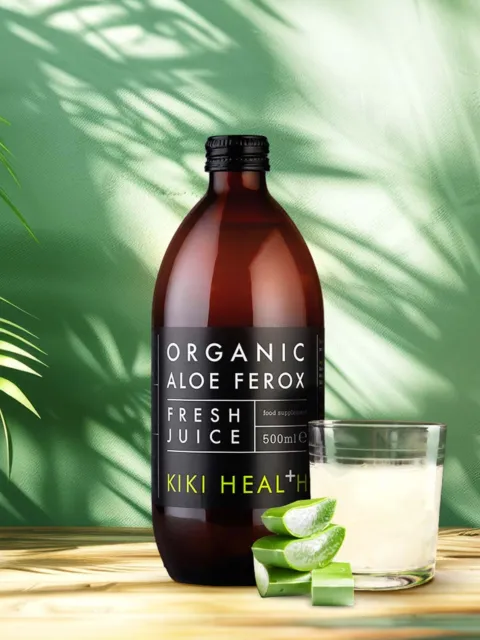 Brown bottle of organic aloe ferox juice, glass, and aloe slices on wooden surface.