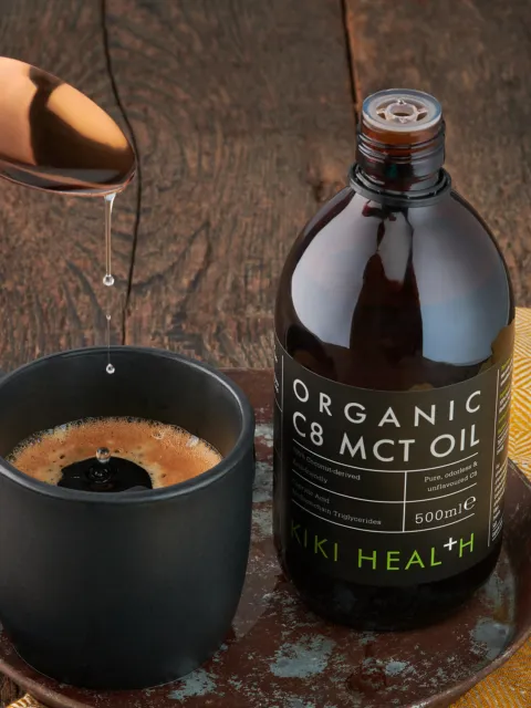 MCT oil bottle beside a mug of coffee on a wooden table.