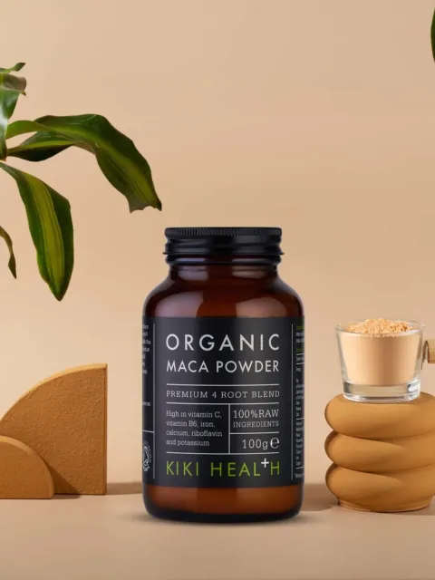 Organic Maca Powder jar, 100g, with a wooden scoop and green leaves in the background.