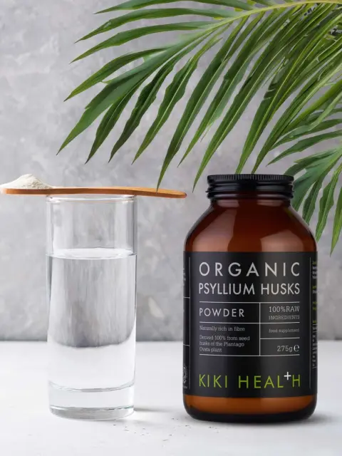 Kiki Health Organic Psyllium Husks jar beside a glass of water and wooden spoon with powder.