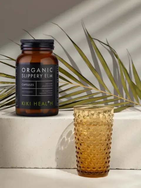 Organic Slippery Elm capsules bottle on stone block with amber glass and palm leaf.
