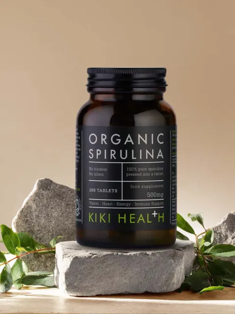 Organic Spirulina tablets by Kiki Health, 200 count, on stone with green leaves.