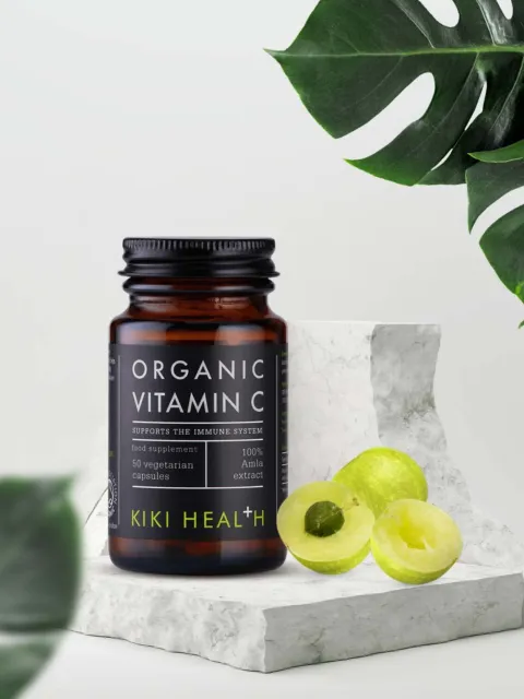 Kiki Health Organic Vitamin C bottle with sliced amla on marble surface, surrounded by green leaves.