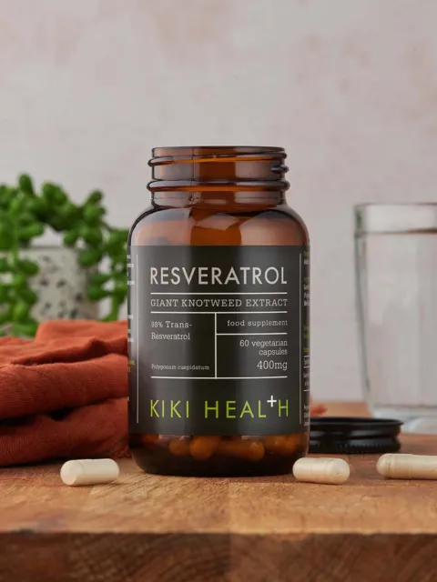 Kiki Health Resveratrol supplement bottle on wooden table with capsules and glass.