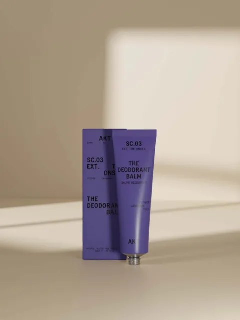 Purple deodorant balm tube and box with text, in soft light.