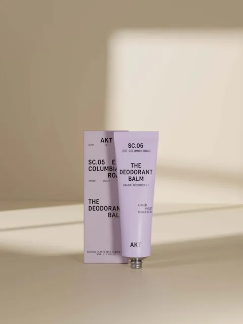 AKT deodorant balm tube and box on a beige surface with soft shadows.