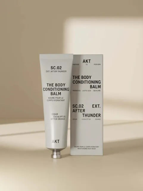 Tube and box of AKT SC.02 Body Conditioning Balm on beige background.