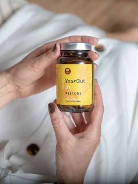 Hands holding a jar of YourGut 01 Restore food supplement capsules.