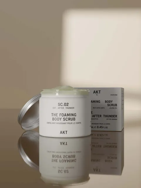 AKT foaming body scrub jar and box on reflective surface.