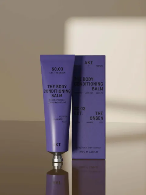 Purple tube and box of AKT SC.03 The Body Conditioning Balm on a reflective surface.
