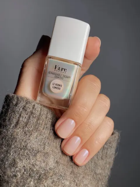 Hand holding Kure Bazaar nail polish bottle, wearing a grey knitted sleeve.