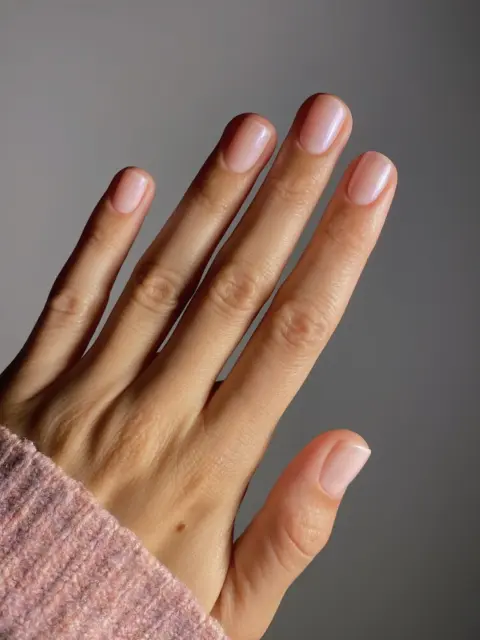 Hand with neatly manicured nails, wearing a pink knitted sleeve.