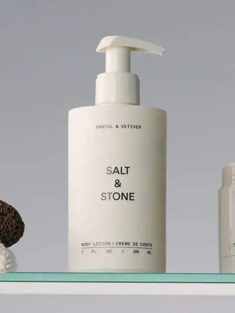 Salt & Stone body lotion and deodorant on a glass shelf with a pumice stone and towel.