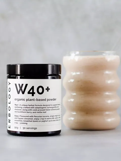W40+ organic plant-based powder jar next to a wavy glass filled with a beige smoothie.