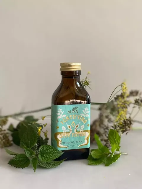 Brown bottle with blue label, "MOA Fortifying Green Potion", surrounded by herbs.