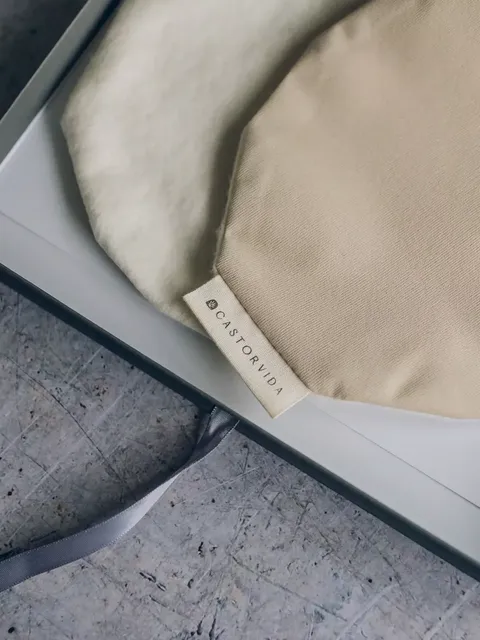 Beige and cream fabric bags with "CASTORVIDA" label in a box on a textured surface.