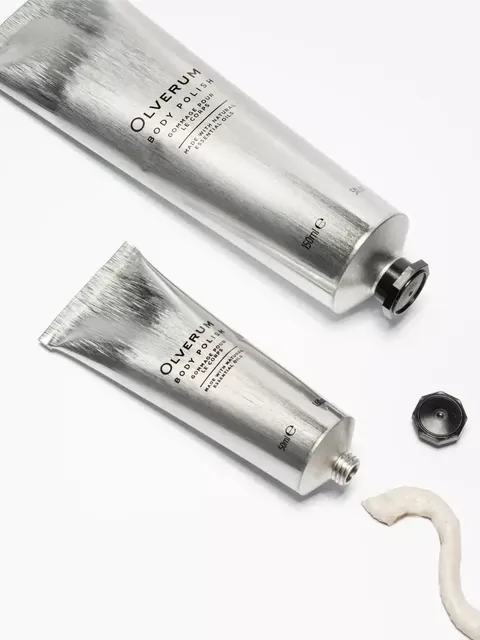 Two silver tubes of Olverum Body Polish on a white background, with cream and a black cap.
