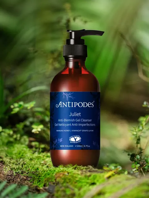 Antipodes Juliet Anti-Blemish Gel Cleanser bottle on a mossy surface with green foliage background.