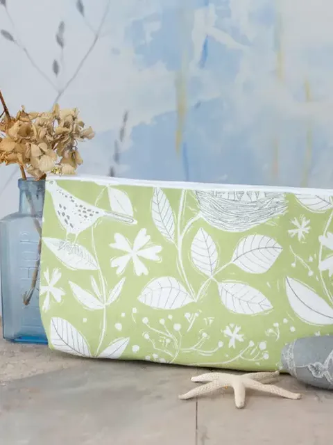 Green floral toiletry bag on wooden table with dried flowers and stones.
