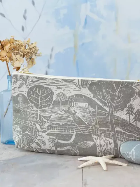 Grey pouch with landscape design, dried flowers in vase, stones, and starfish on wooden surface.