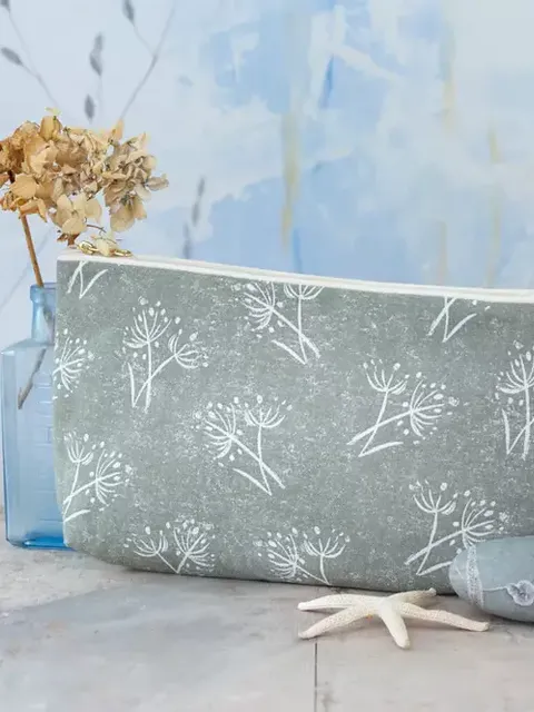 Green pouch with white floral pattern, beside dried flowers in a blue vase and grey stones.