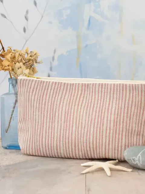 Striped fabric pouch on wooden table with dried flowers and stones.