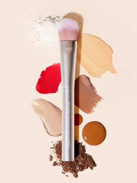 Makeup brush with various coloured powders and creams on a beige background.