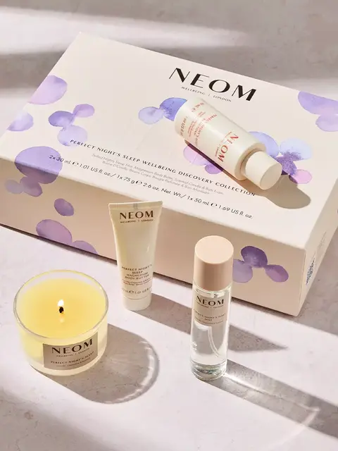 Neom Perfect Night's Sleep set with candle, cream, and spray on a light surface.