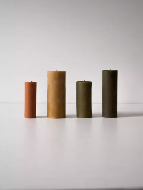 Four pillar candles in varying heights and earthy tones on a white surface.
