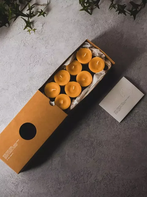 Box of eight yellow candles on grey surface with green ivy.