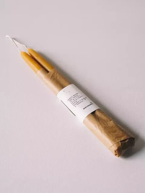 Two yellow candles wrapped in brown paper with a white label on a light surface.
