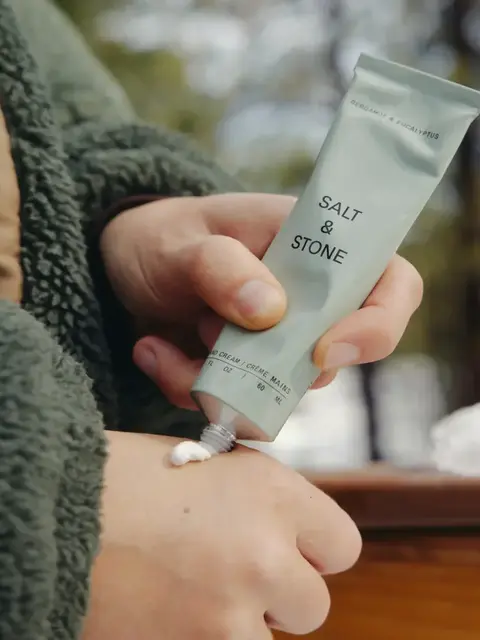 Person applying Salt & Stone hand cream outdoors.