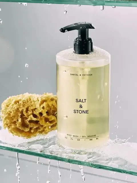 Salt & Stone body wash with sponge on wet glass shelf.