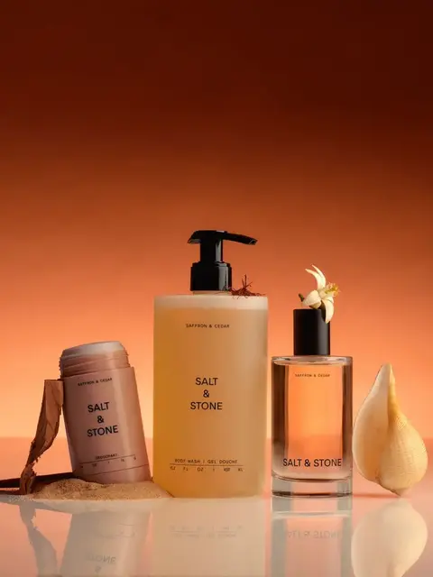 Salt & Stone skincare products on reflective surface, orange background.