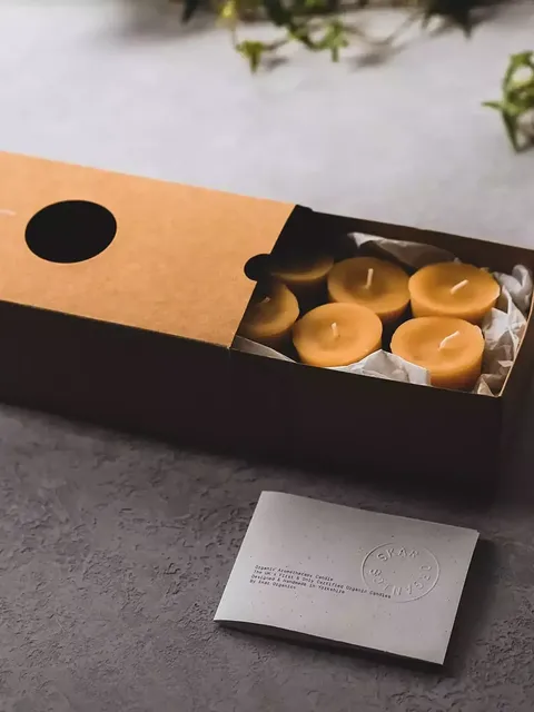 Brown box with six yellow candles, card with embossed text, and green ivy in the background.