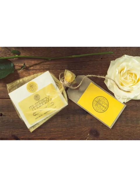 Skincare product with yellow label, gift tag, and white rose on wooden surface.