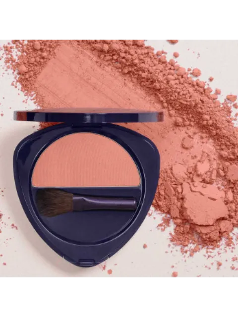 Open compact with peach blush and brush, surrounded by loose powder.