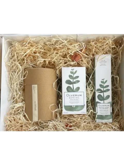 Gift box with Olverum bath oil, pillow mist, and a brown cylindrical package on straw.