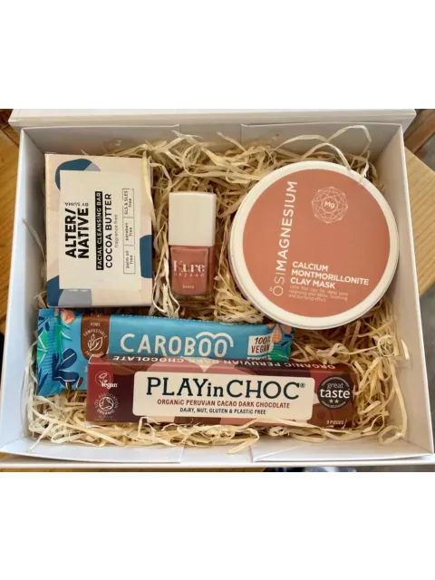 Gift box with clay mask, cleansing bar, nail polish, and vegan chocolate bars on straw filling.