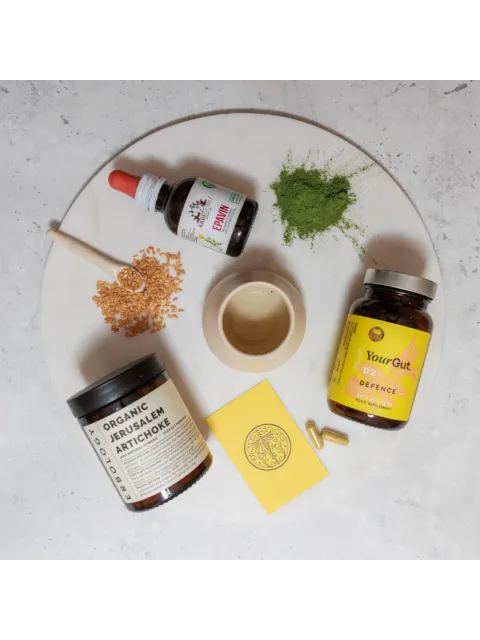 Supplements, flax seeds, green powder, and a small bowl on a round white surface.