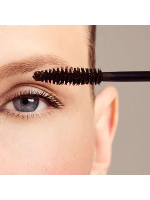 Close-up of a mascara wand near an eye with long lashes.