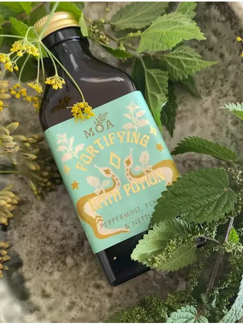 Fortifying bath potion bottle with peppermint, fennel, and nettle, surrounded by green leaves.