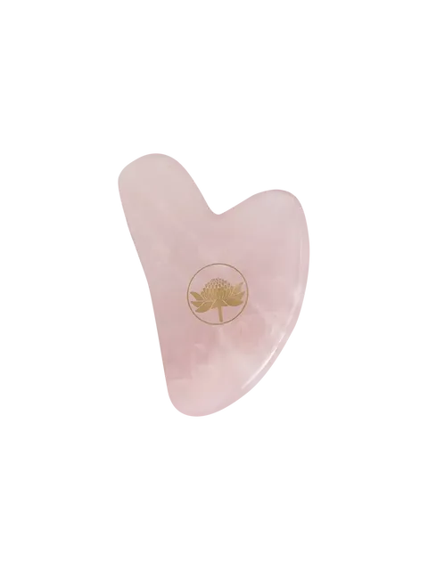 Pink heart-shaped gua sha tool with a gold floral logo.